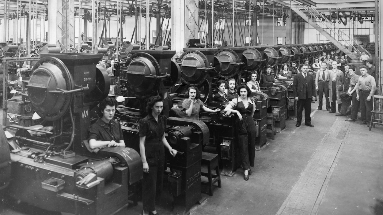 Des hommes et des femmes sont adossés à des machines dans cette photo en noir et blanc.