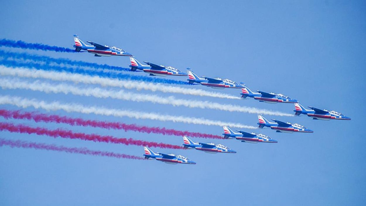 Des avions bleu, blanc et rouge volent en escadrille avec de la fumée tricolore qui sort dans leur sillage.