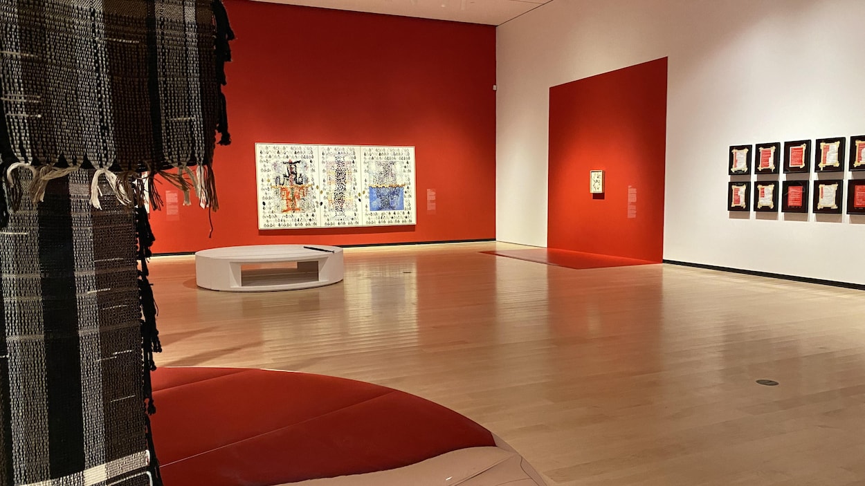 Une grande salle d'exposition où il y a des tableaux de différentes grandeurs aux murs. À l'avant-plan à gauche, des tissus noir et blanc sont suspendus et un grand cercle un miroir recouvre une partie du sol. 