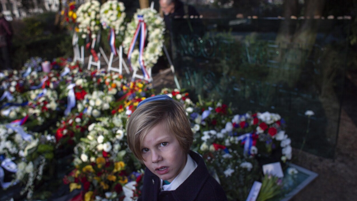 Un garçonnet portant une kippa devant un tapis de bouquets et de couronnes de fleurs.