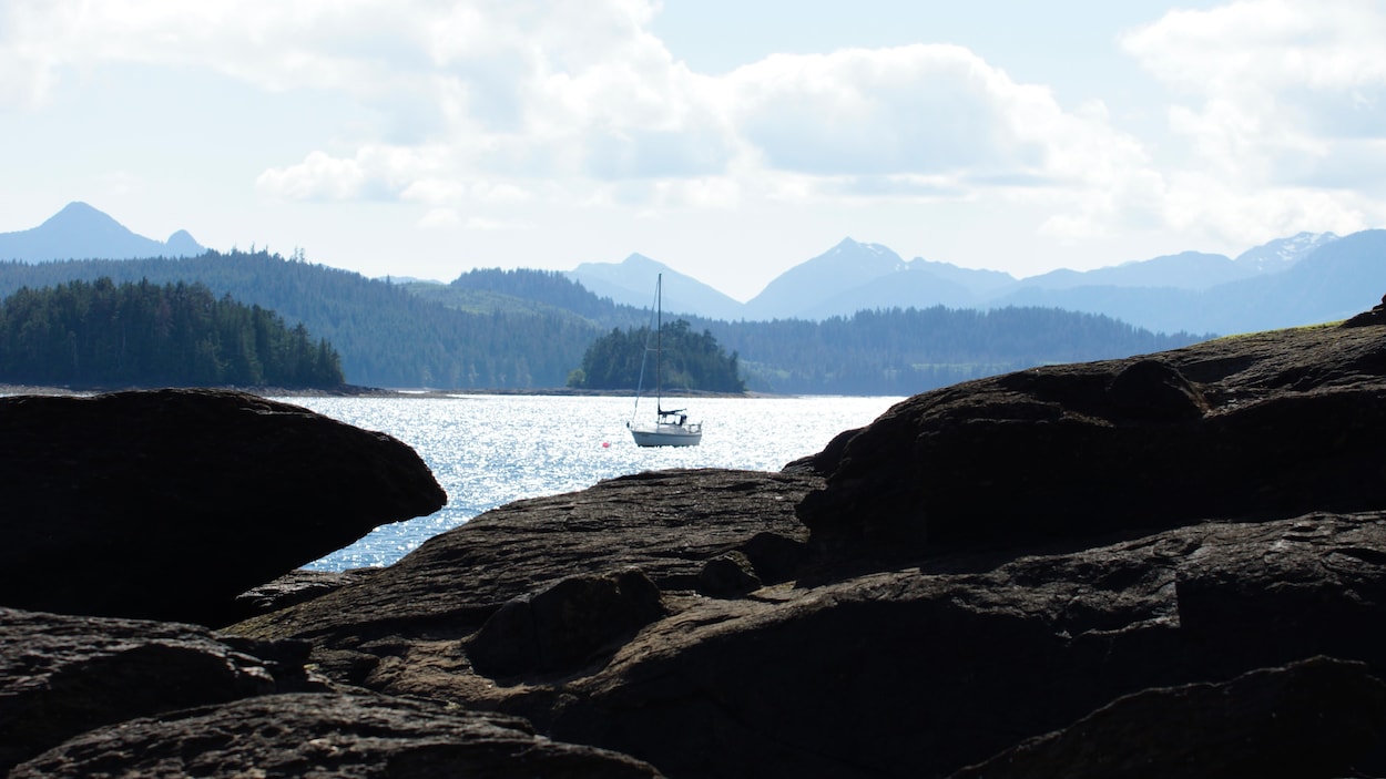 Un paysage marin, avec un voilier et des montagnes à l'horizon.