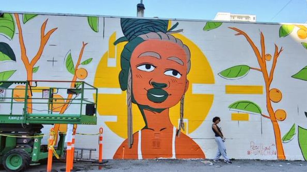 L'artiste Pearl Low est debout devant sa peinture murale et à côté d'un ascenseur hydraulique.