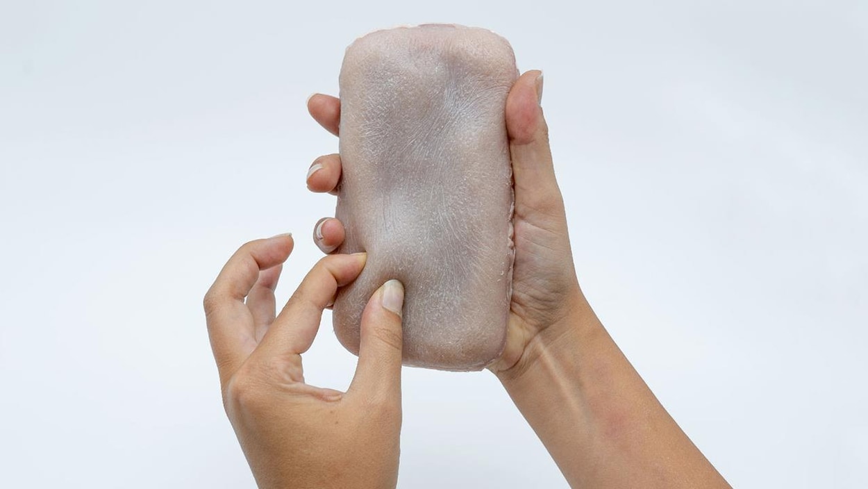 Des mains tiennent un iPhone recouvert d'une membrane ressemblant à de la peau humaine. 