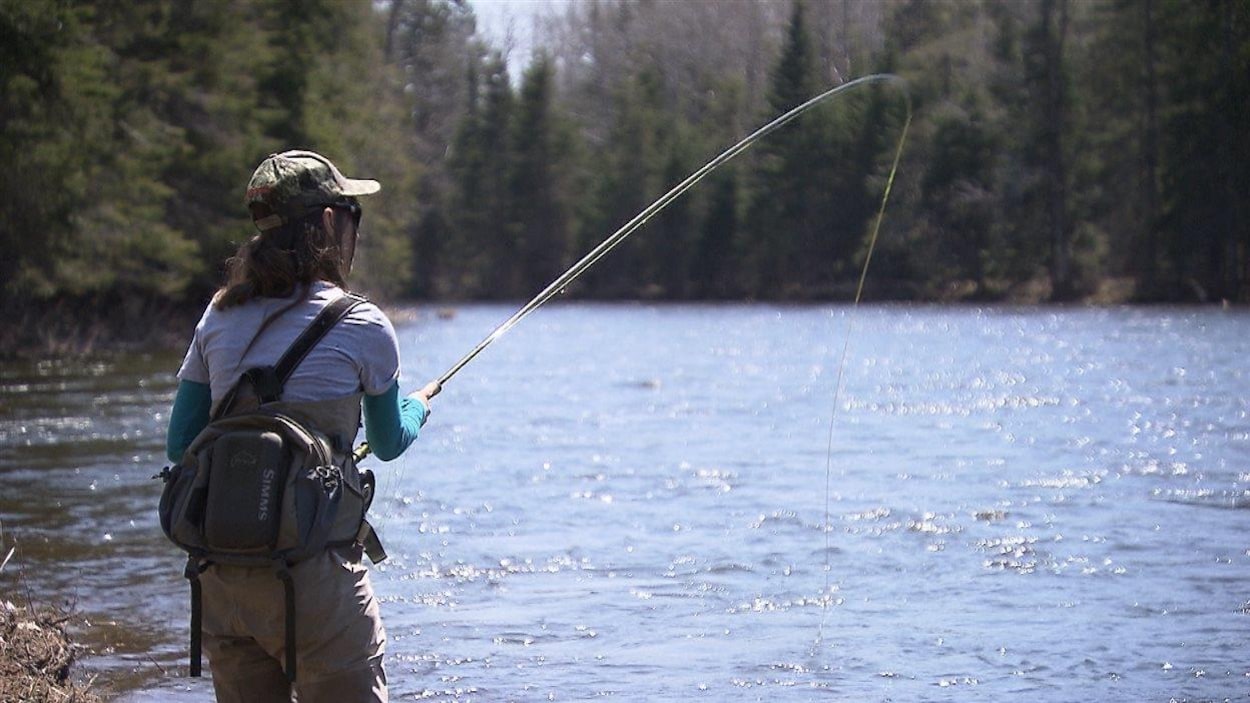 Une femme pêche sur le bord d'une rivière.
