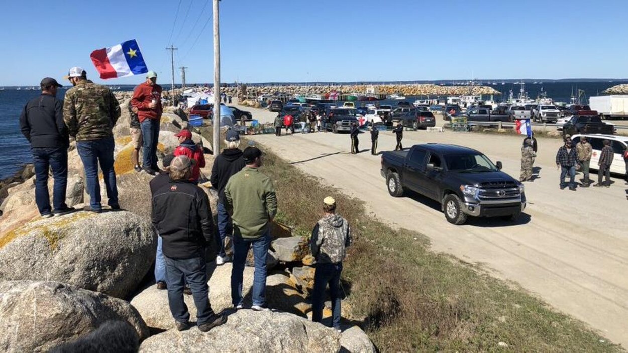 Groupe de pêcheurs, certains tenant des drapeaux acadiens, près d'un quai.