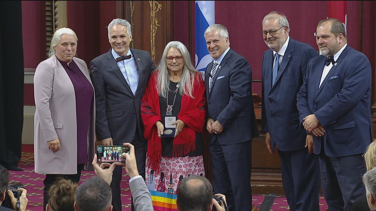 Pénélope Guay, tenant sa médaille dans ses mains, entourée de députés à l'Assemblée nationale.