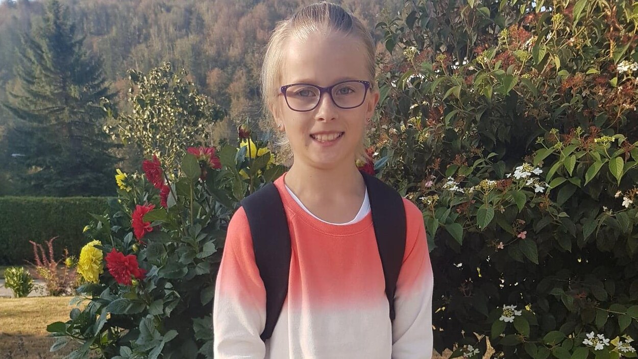 Une jeune fille de 9 ans, blonde avec des lunettes noires, et un chandail rouge, blanc et bleu.