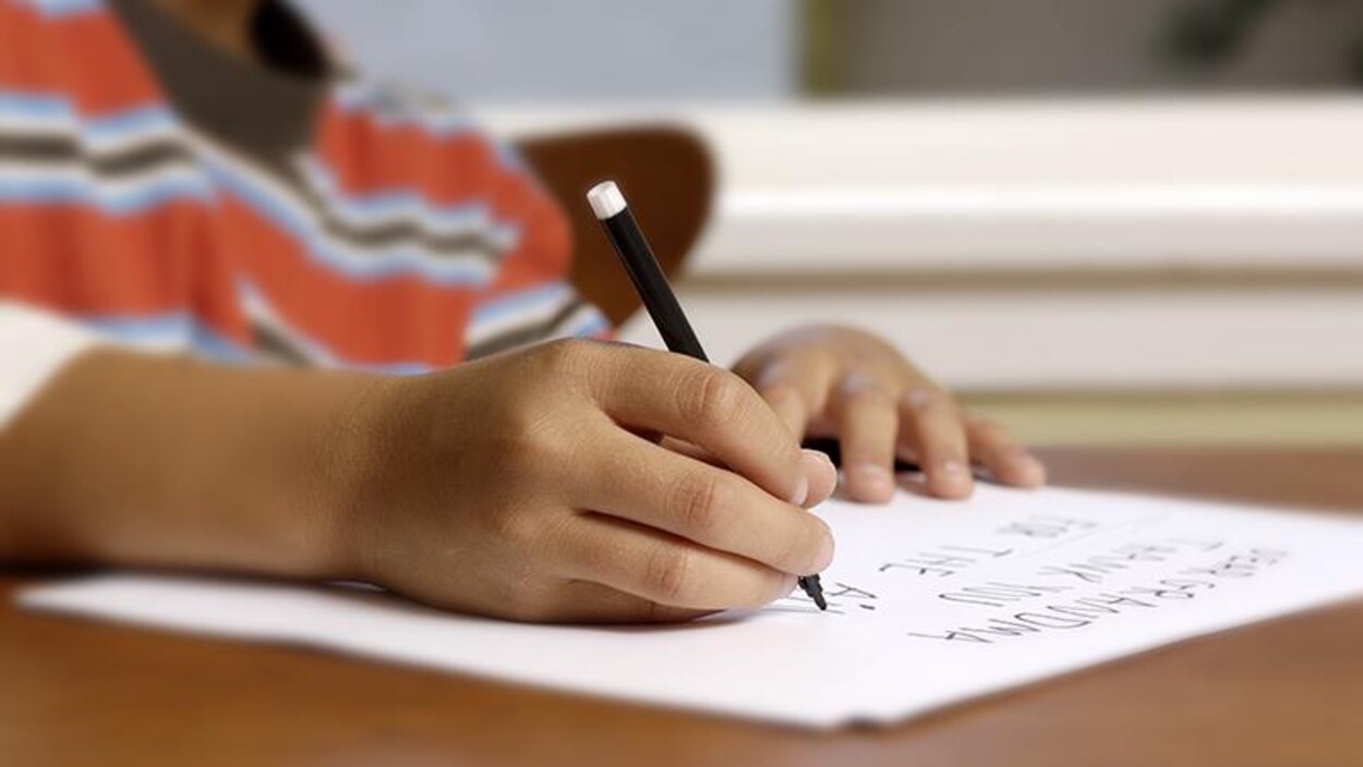 On voit les mains d'un enfant qui écrit sur une feuille.