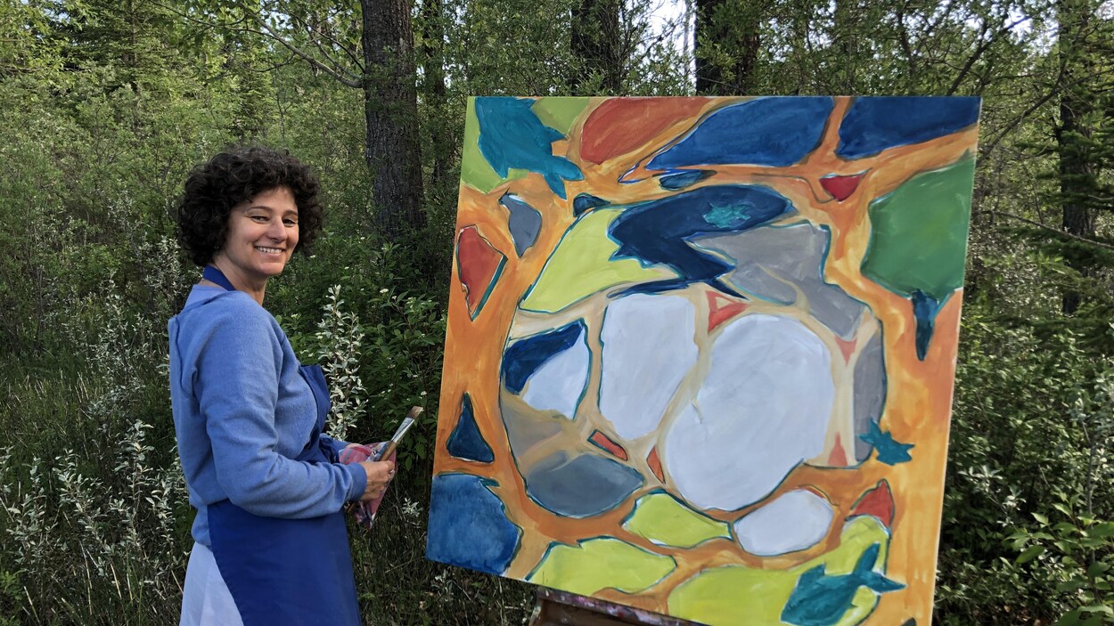 Patricia Lortie dans une forêt est en train de peindre une toile déposée sur un chevalet.