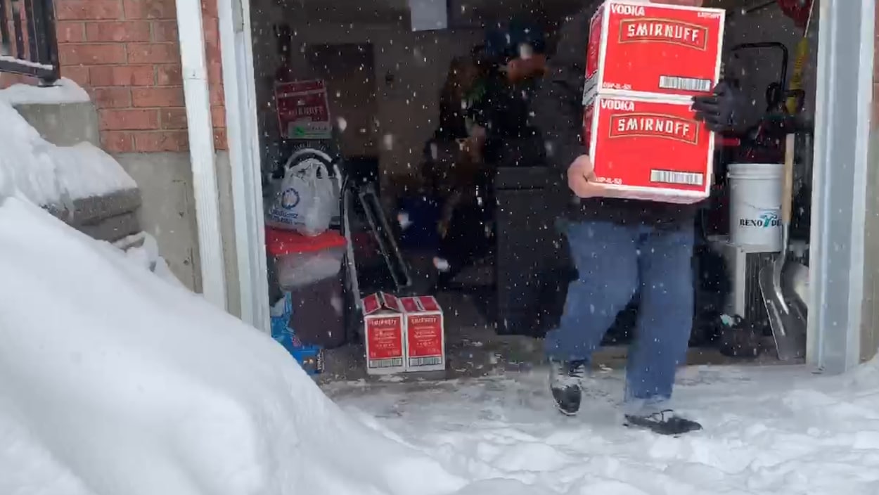 Des hommes sortent des caisses de vodka Smirnoff d'un garage.