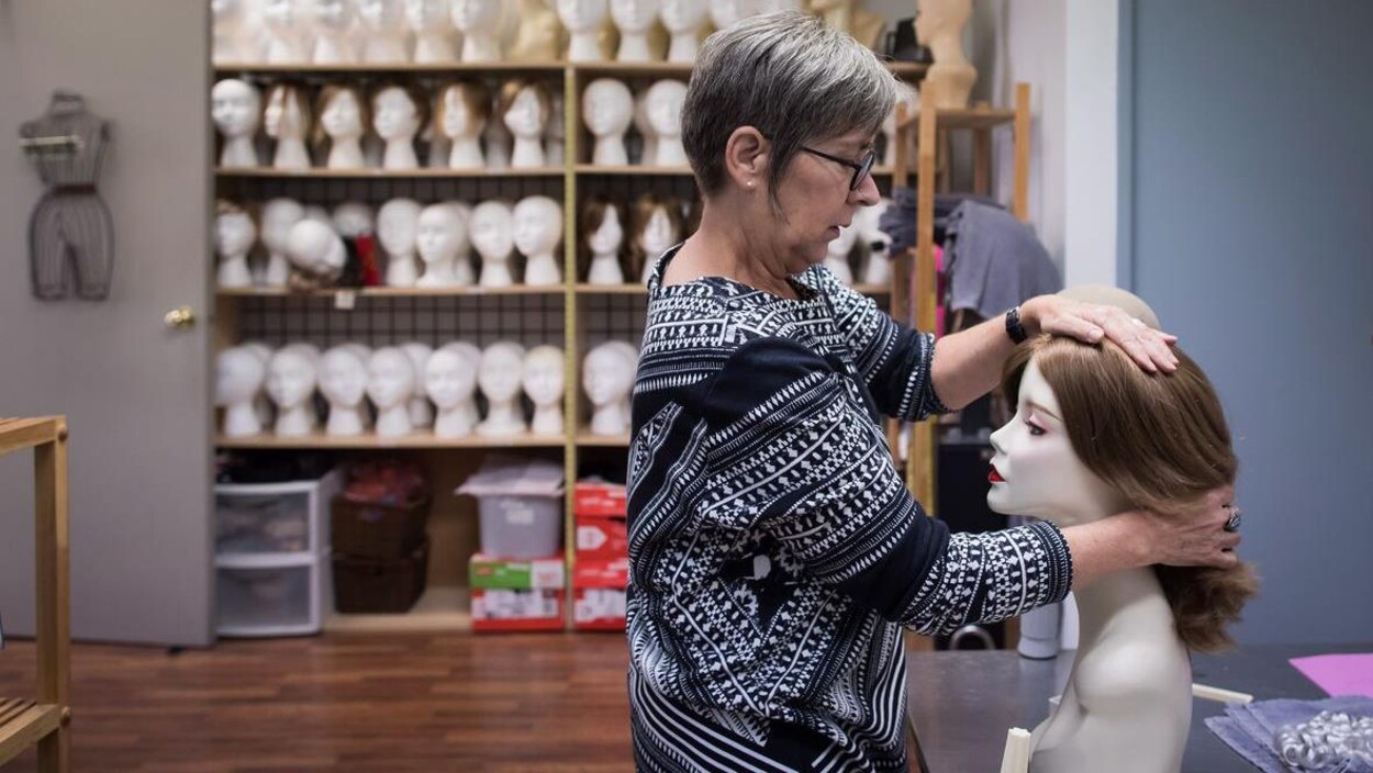 Une femme de profil pose une perruque sur une tête de mannequin.