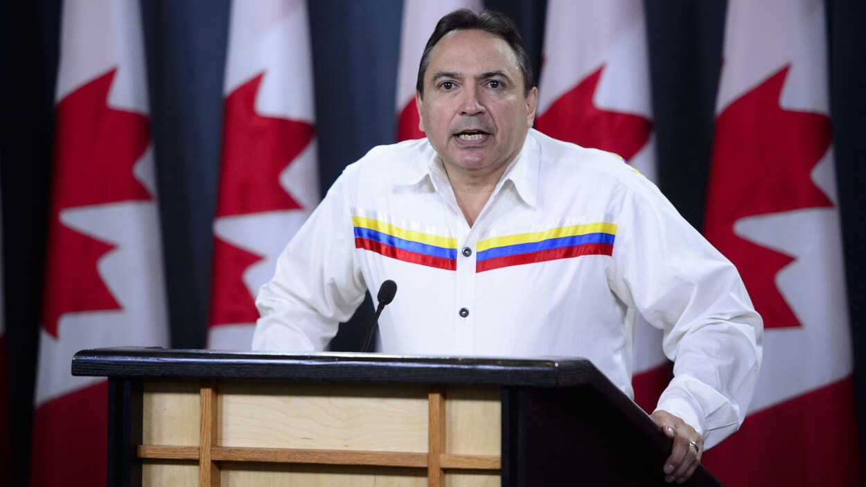 Perry Bellegarde parle devant une série de drapeaux canadiens.