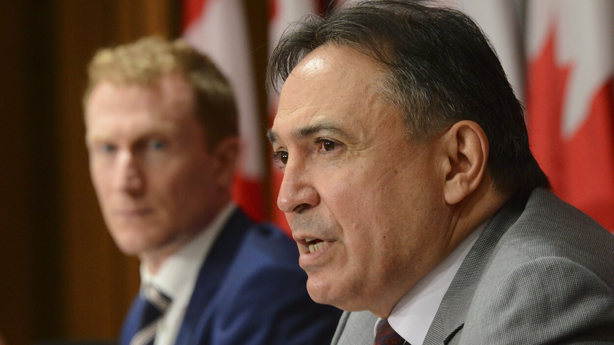 Les deux hommes lors d'une conférence de presse. Des drapeaux canadiens sont installés derrière eux.