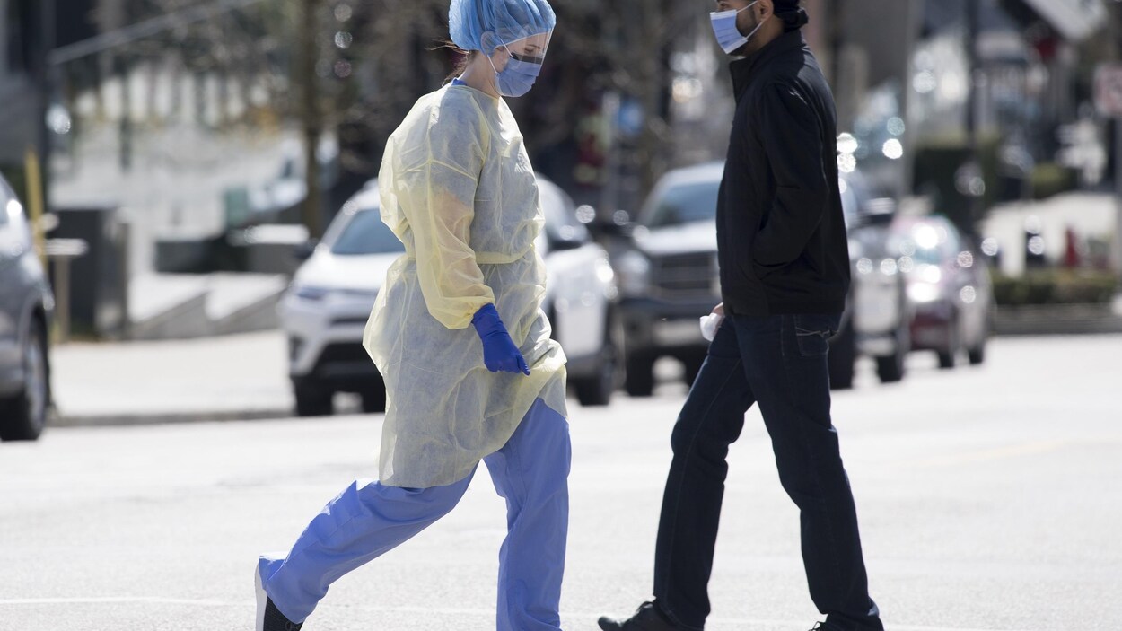 Un travailleur de la santé portant un équipement de protection individuelle complet traverse la rue devant l'hôpital Royal Columbian à New Westminster, en Colombie-Britannique.