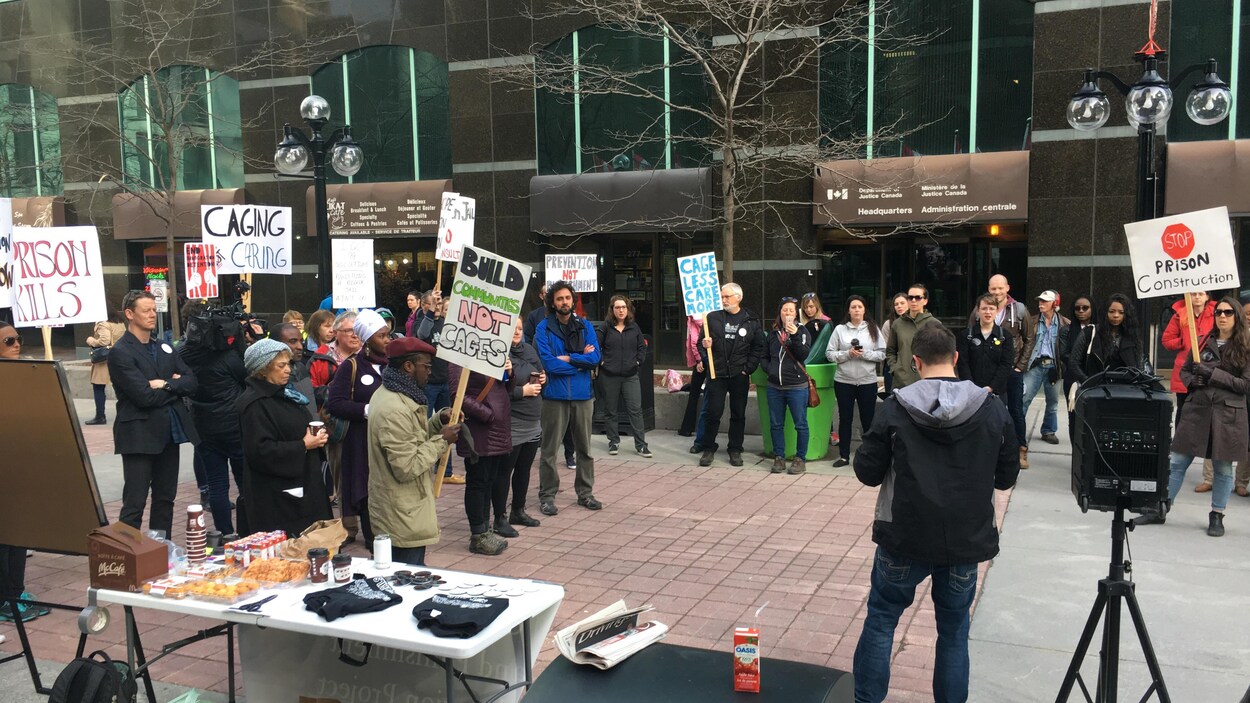 Des personnes devant un édifice tiennent des pancartes. Des personnes devant un édifice tiennent des pancartes.