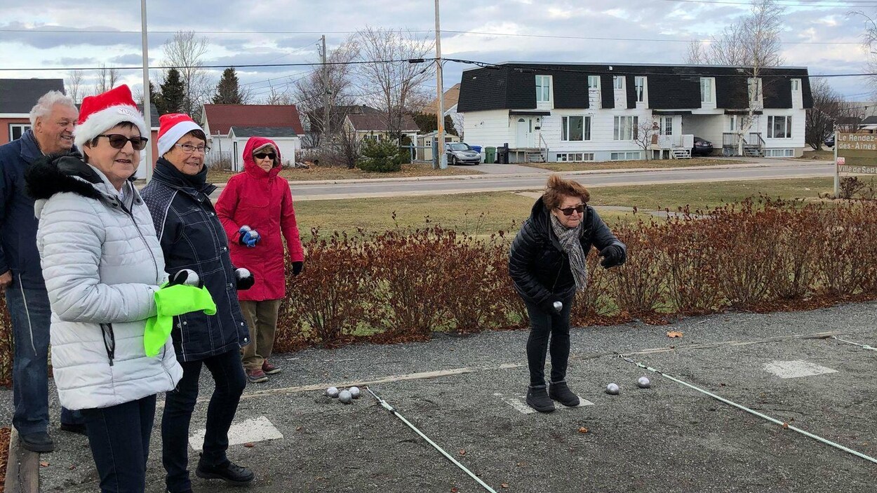 Une femme lance une boule de pétanque. Plusieurs autres la regardent.
