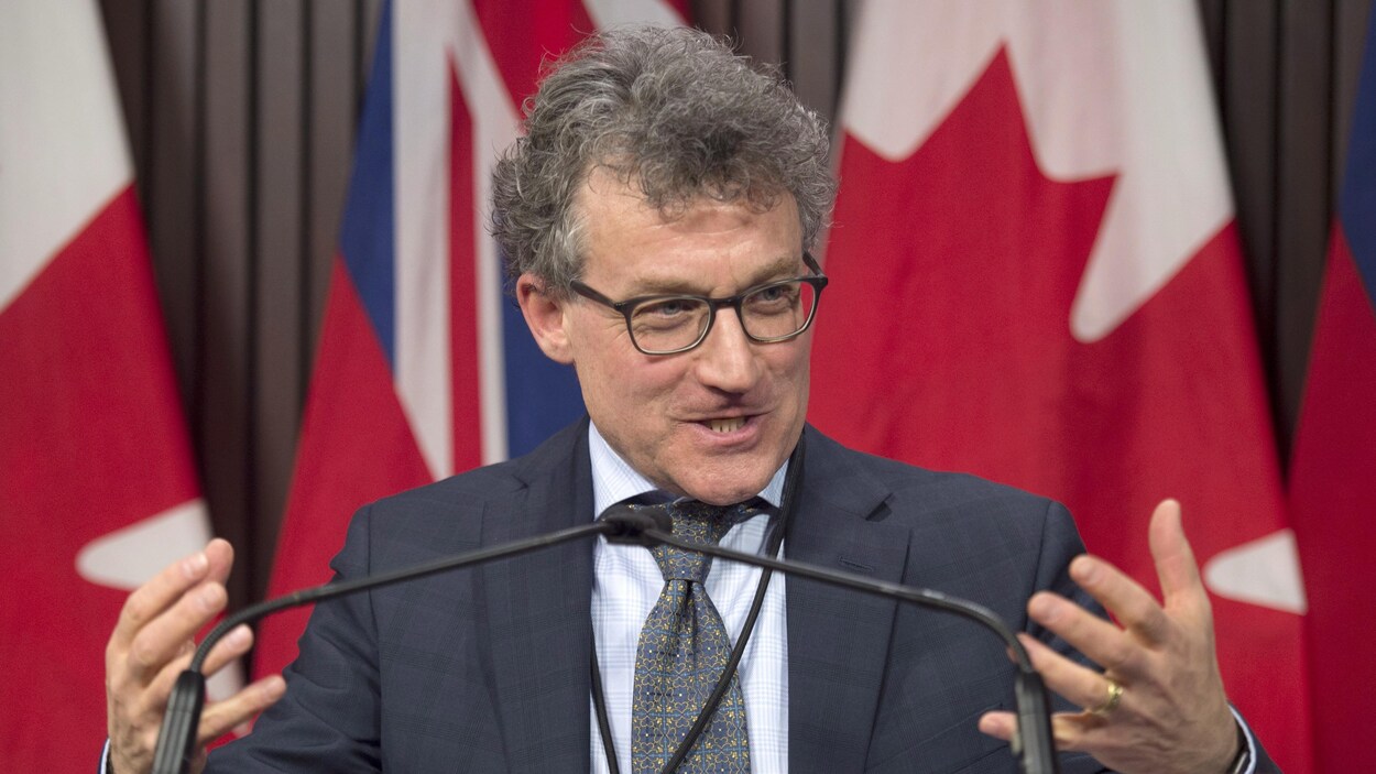 Photo d'un homme portant des lunettes devant des microphones