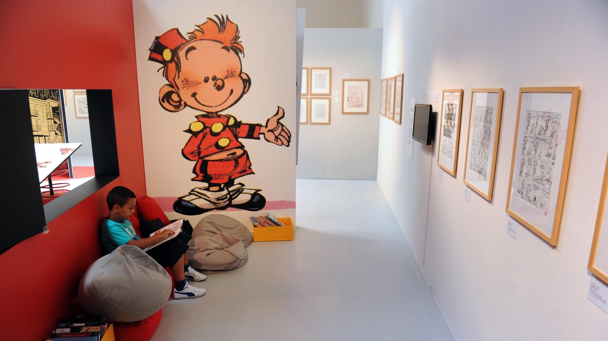 Un enfant lit une bande dessinée du Petit Spirou devant une affiche du personnage.