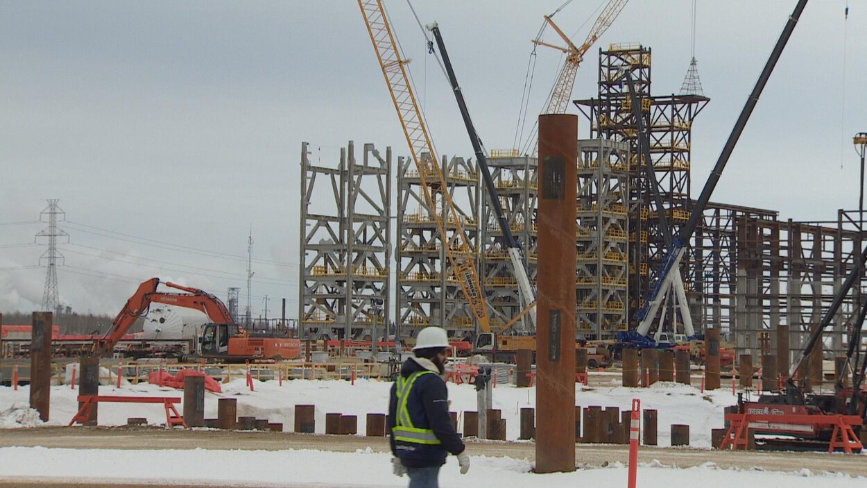 Vue sur un chantier de construction. Il y a un travailleur avec un casque qui marche.