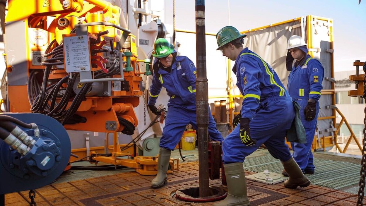 Trois employés du secteur pétrolier travaillent avec une machine à forer.