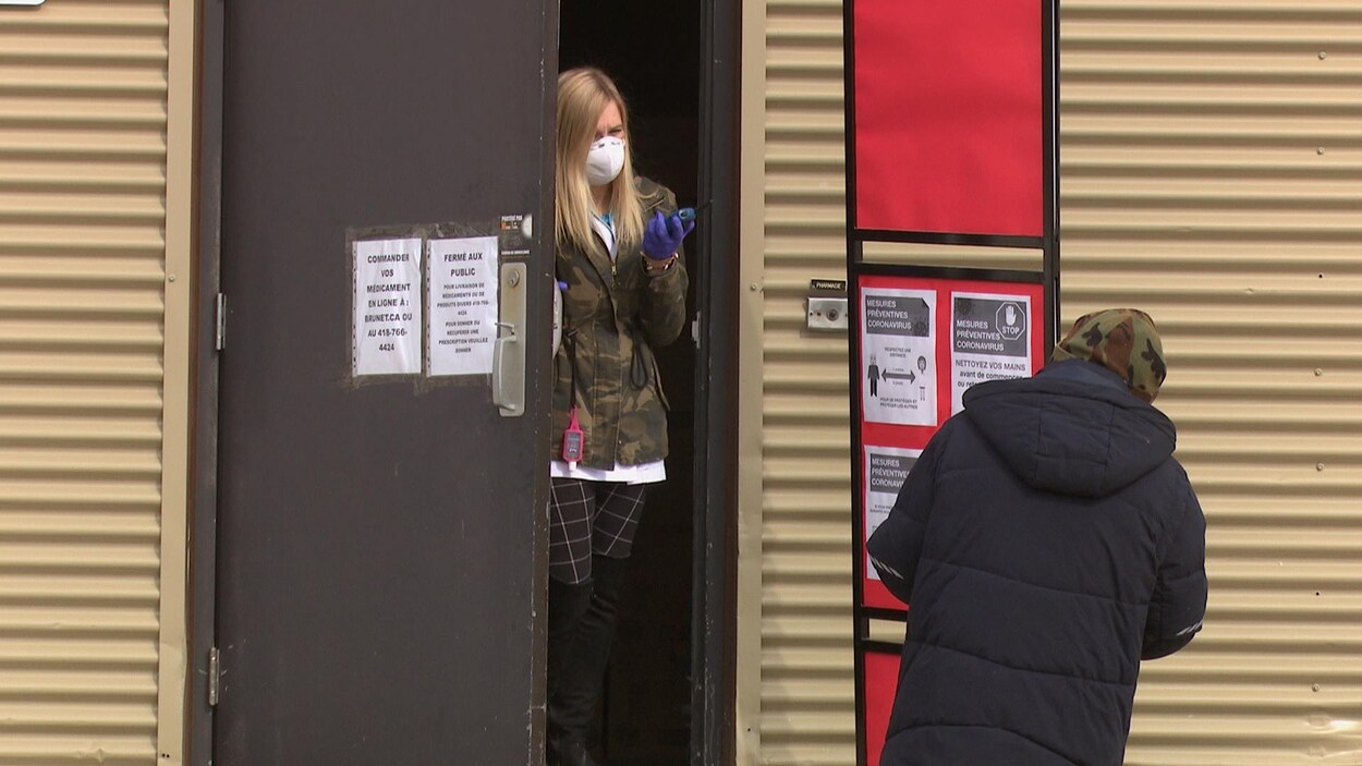Une jeune femme qui porte un masque et des gants parle à un homme à travers une porte entrouverte