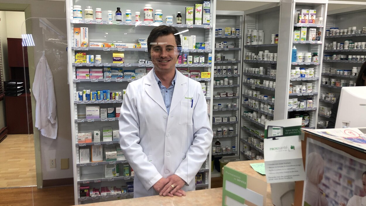 Le pharmacien Nicolas Huot est debout derrière un écran protecteur au comptoir des ordonnances.