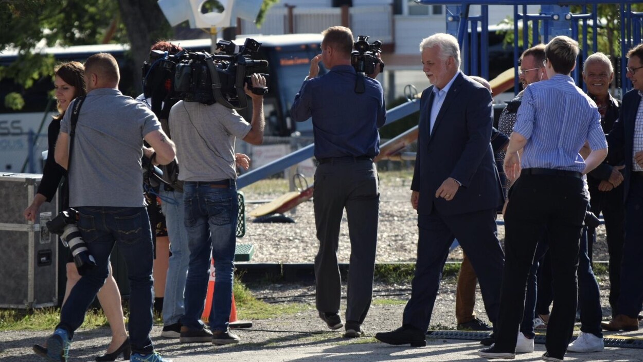 Philippe Couillard sur le terrain d'une école avec des journalistes