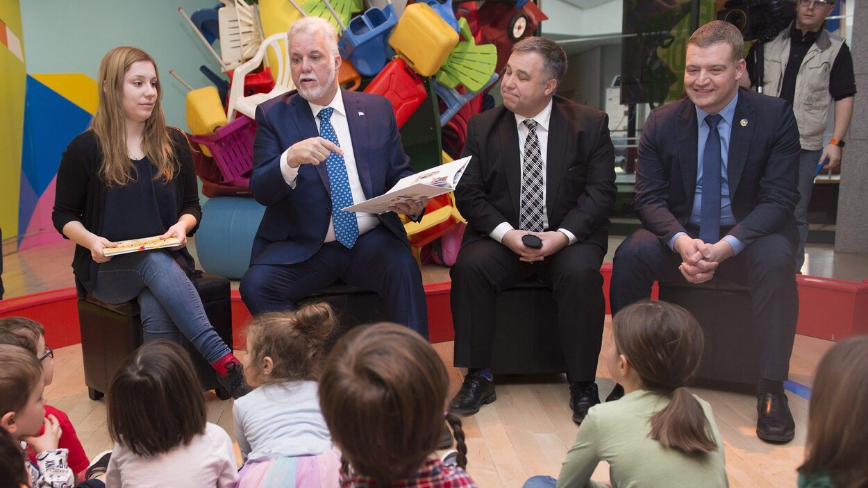 Le premier ministre Philippe Couillard et les ministres de l'Éducation, Sébastien Proulx, et de la Famille, Luc Fortin, sont assis devant des enfants.