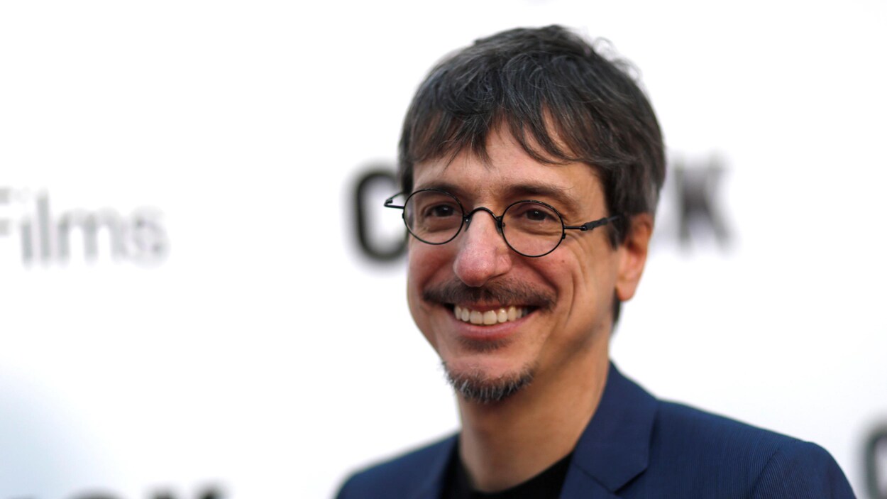 Philippe Falardeau, vêtu d'un veston, prend la pose devant des caméras.