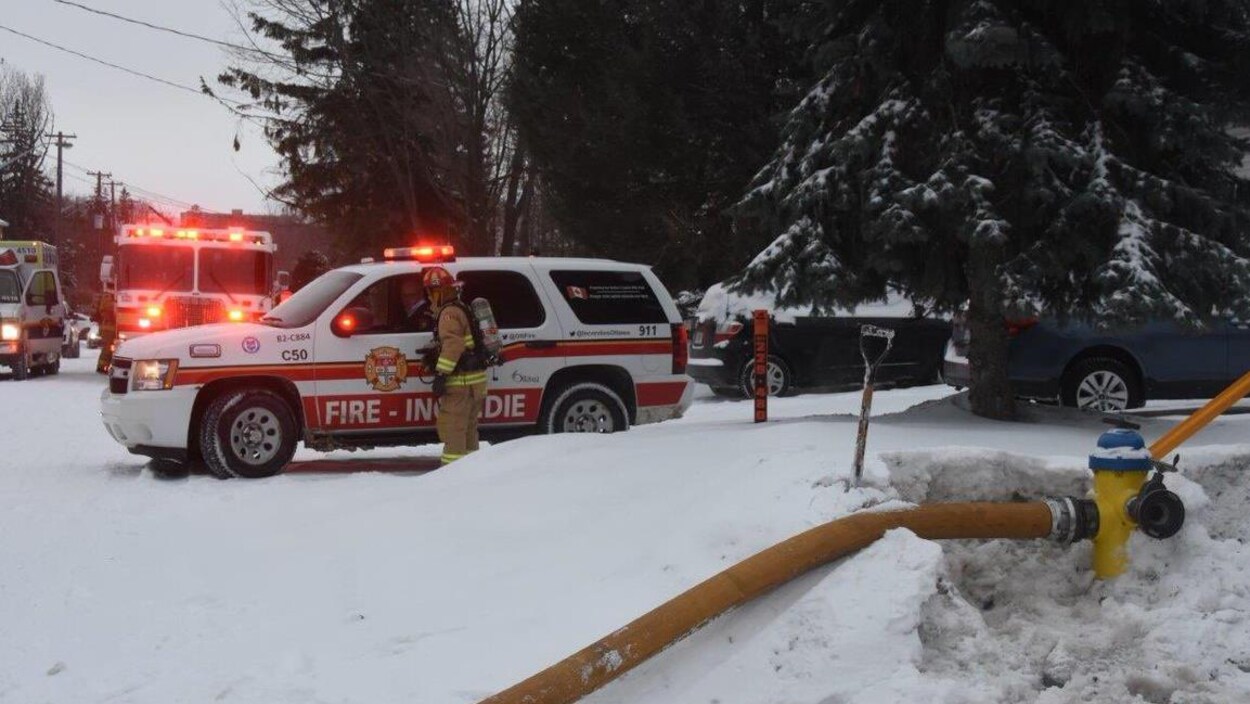 Une borne fontaine est entourée de neige. Des véhicules du Service des incendies d'Ottawa se trouvent derrière. Une borne fontaine est entourée de neige. Des véhicules du Service des incendies d'Ottawa se trouvent derrière.