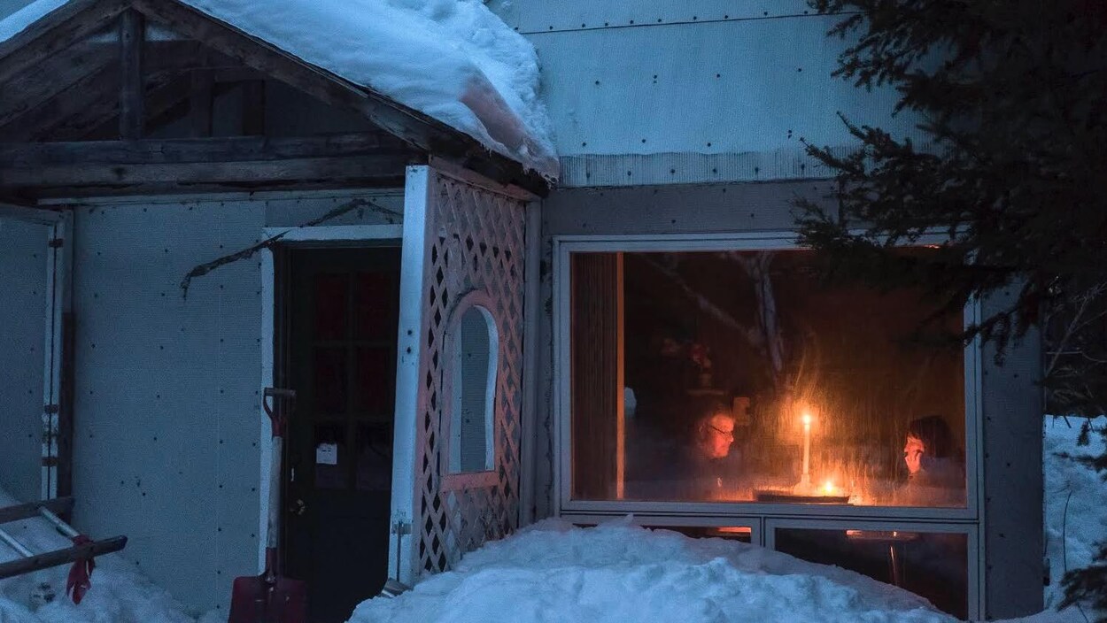 Devant la façade d'une petite maison, un couple éclairé à la chandelle se fait face.