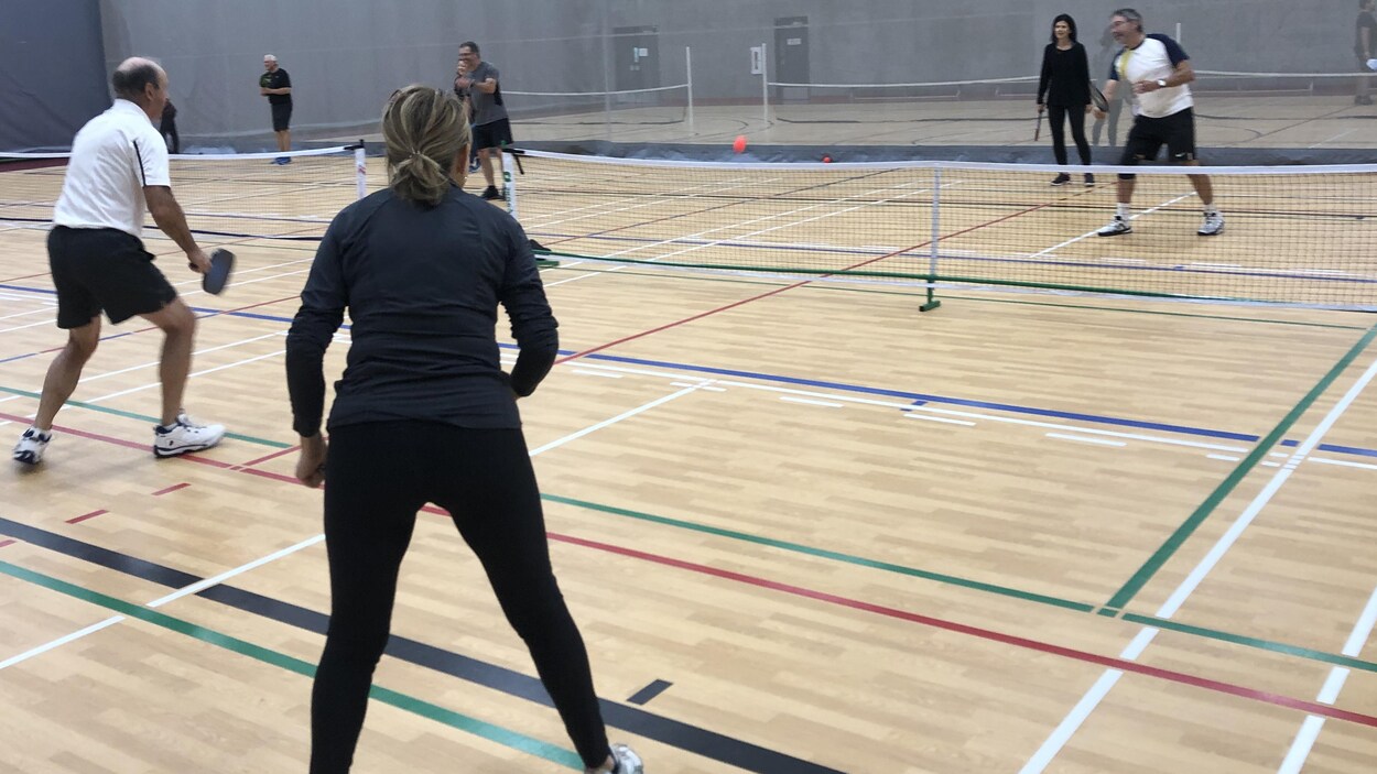 Deux personnes de chaque côté du filet se font des passes dans un gymnase.