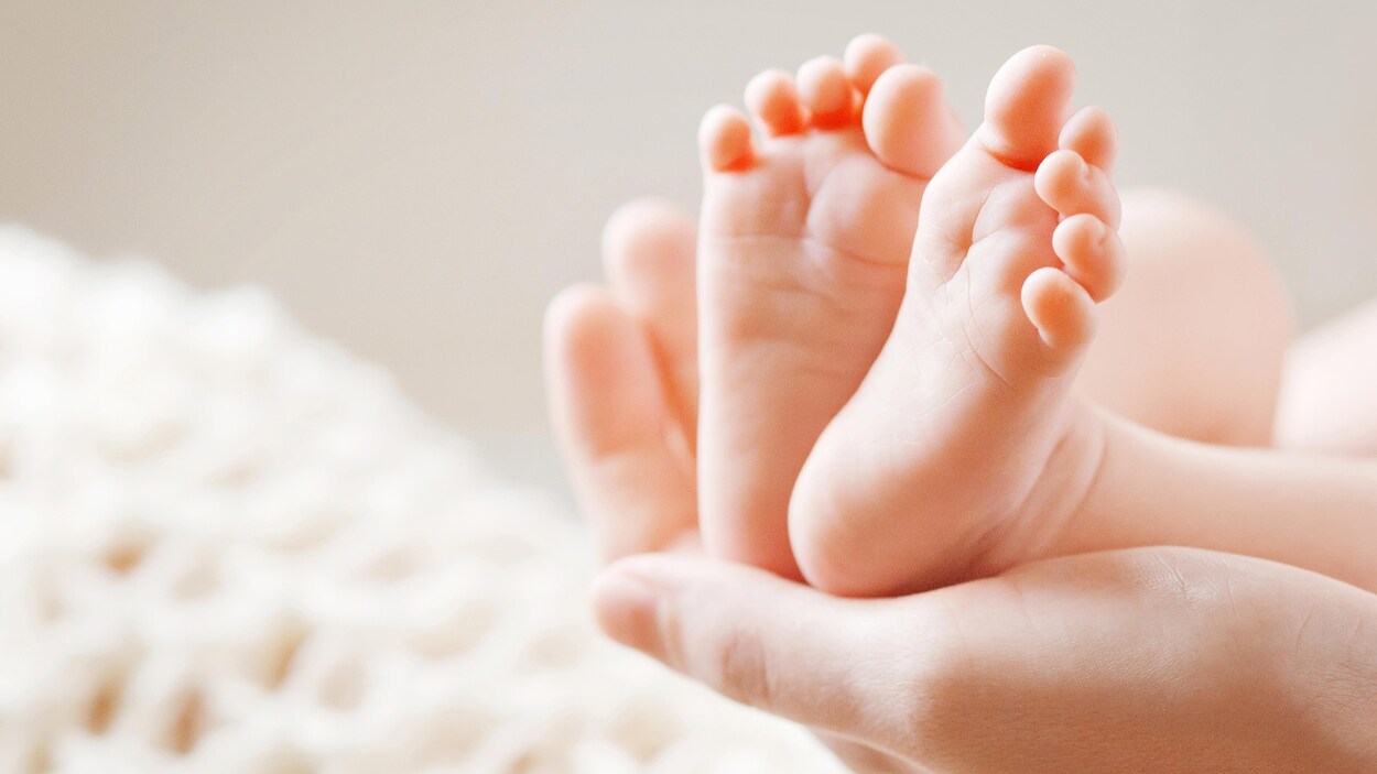 Les pieds d'un bébé sont posés dans la main d'une personne. Les petits pieds et la main sont très bien éclairés.