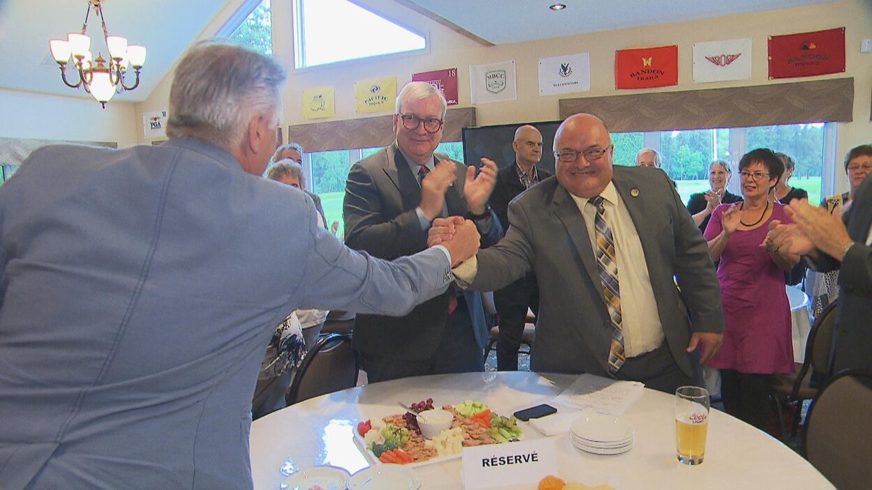 Pierre Giguère aux côtés du ministre Luc Blanchette qui serre la main de Laurent Lessard par-dessus une table, au club de golf de Grand-Mère