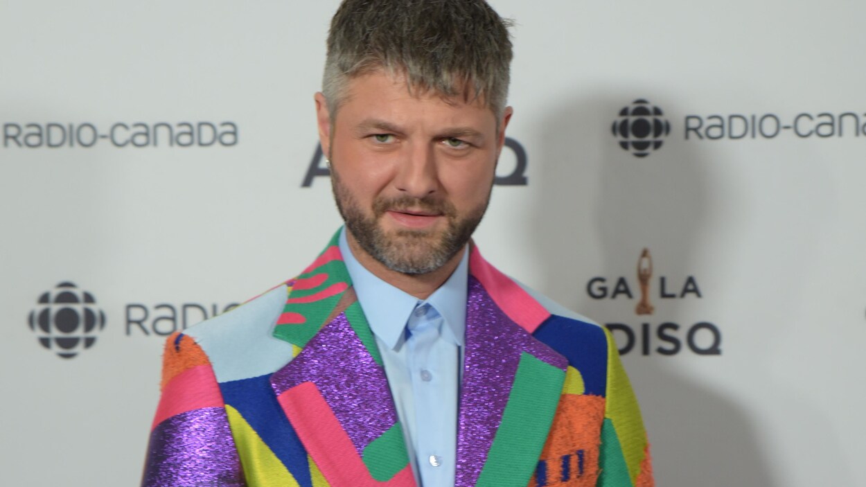 Le chanteur est vêtu d'un veston de couleurs différentes.