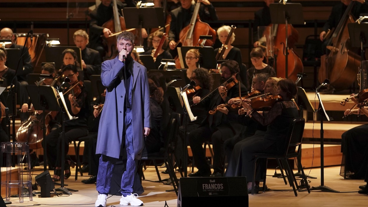 Un chanteur est accompagné d'un orchestre complet sur scène.