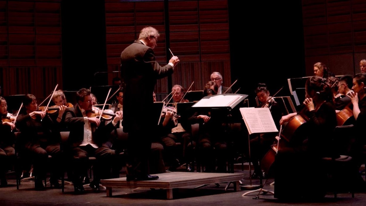 Maestro Pierre Simard devant les musiciens du Vancouver Island Symphony.Tout juste derrière le chef d'orchestre, la section des cordes.
