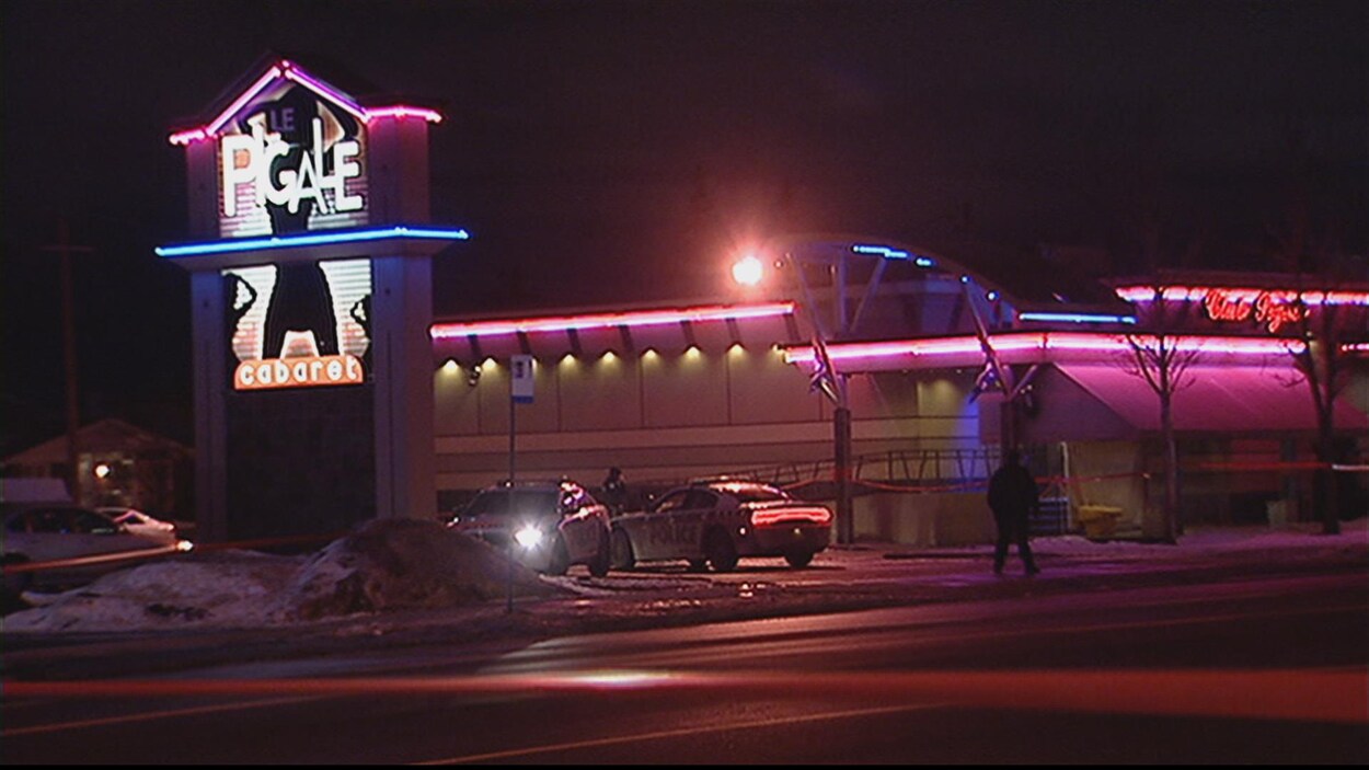 Une photo du club Le Pigale prise la nuit, deux voitures de police et deux silhouettes dans le stationnement Une photo du club Le Pigale prise la nuit, deux voitures de police et deux silhouettes dans le stationnement