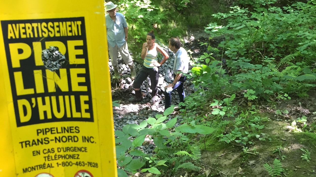 Sylvie Rozon se tient derrière une affiche jaune qui indique la présence d'un pipeline de Trans-Nord inc. dans un boisé de Saint-Lazare.