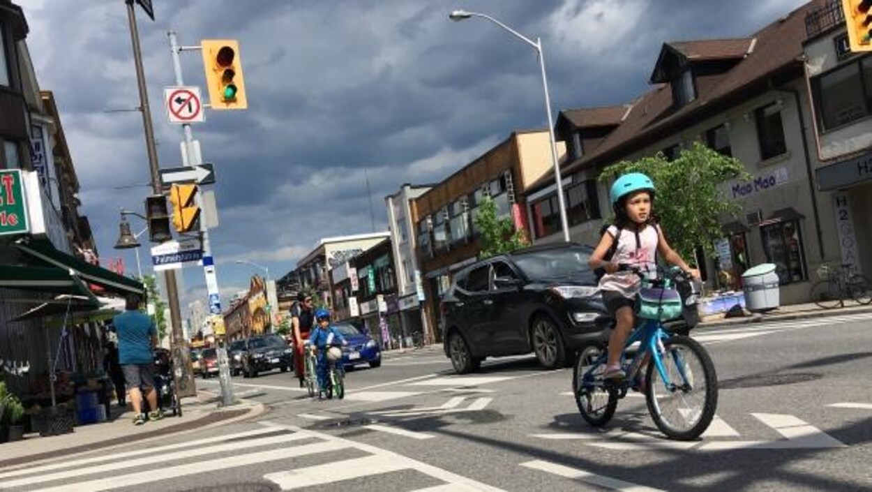 Photo d'une fillette qui roule sur la piste cyclable devant son frère et son père.