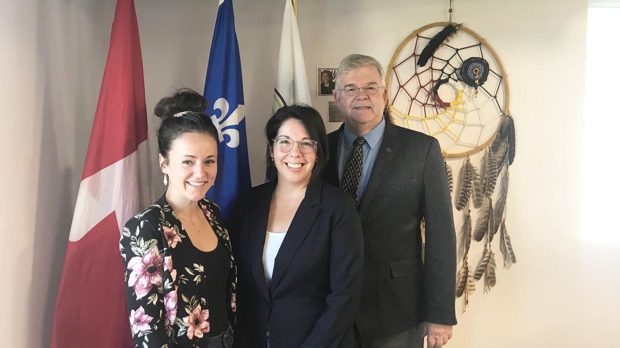 Mélanie Racette et Pierre Corbeil posent devant les drapeaux du Québec et du Canada et un capteur de rêve.