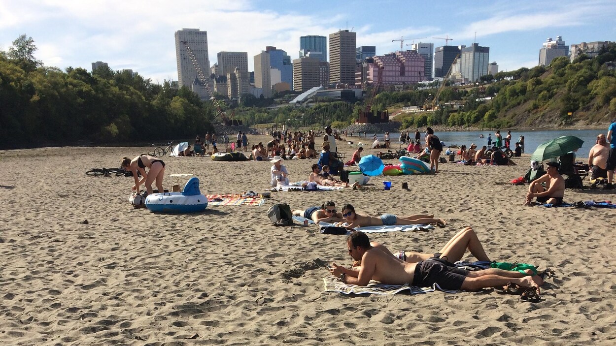 Des personnes en maillot de bain prennent le soleil sur la plage de sable fin située le long de la rivière Saskatchewan Nord. En arrière-plan, la présence d'édifices montre que le centre-ville n'est pas loin. Des personnes en maillot de bain prennent le soleil sur la plage de sable fin située le long de la rivière Saskatchewan Nord. En arrière-plan, la présence d'édifices montre que le centre-ville n'est pas loin.