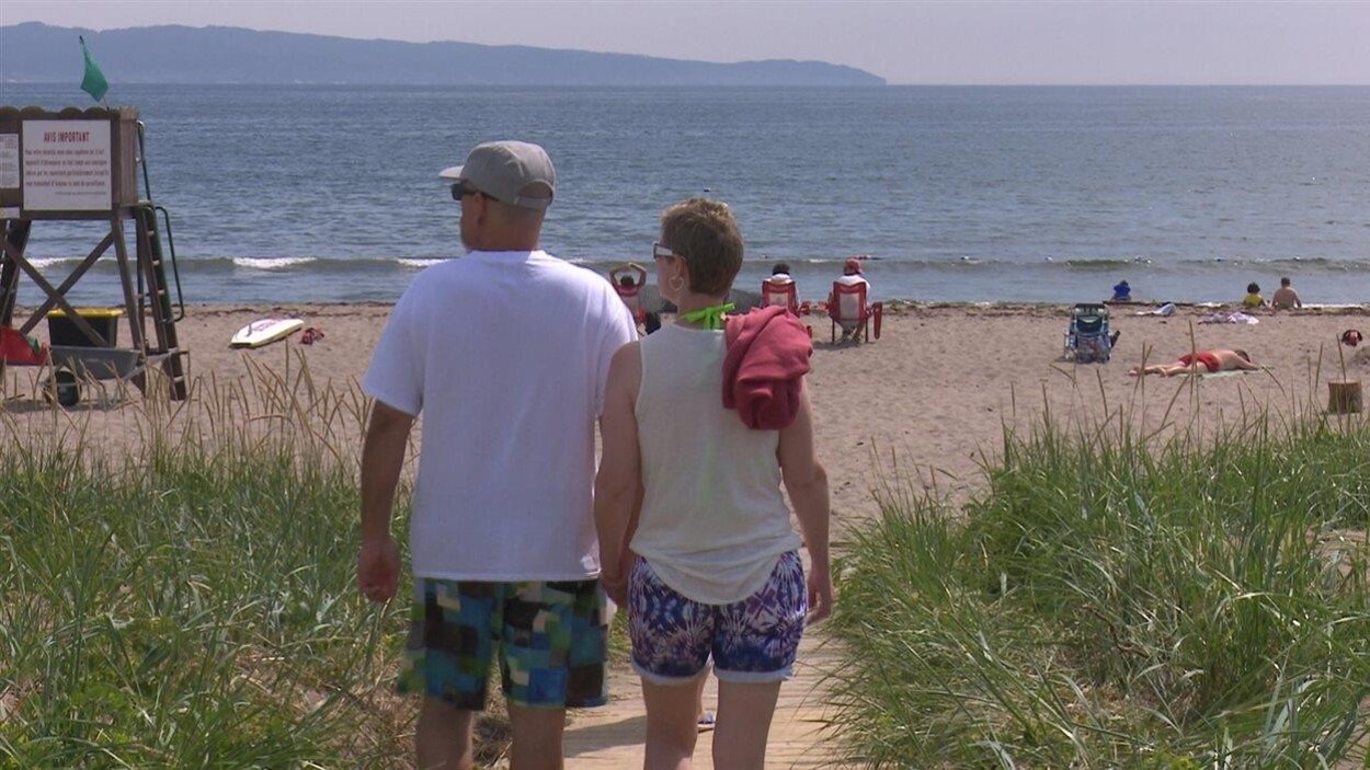 Un homme et une femme marchent vers une plage où se trouvent aussi d'autres personnes qui profitent des lieux.