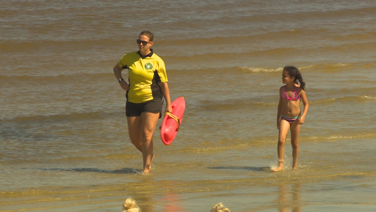 Un agent de sécurité arpente une plage avec une enfant