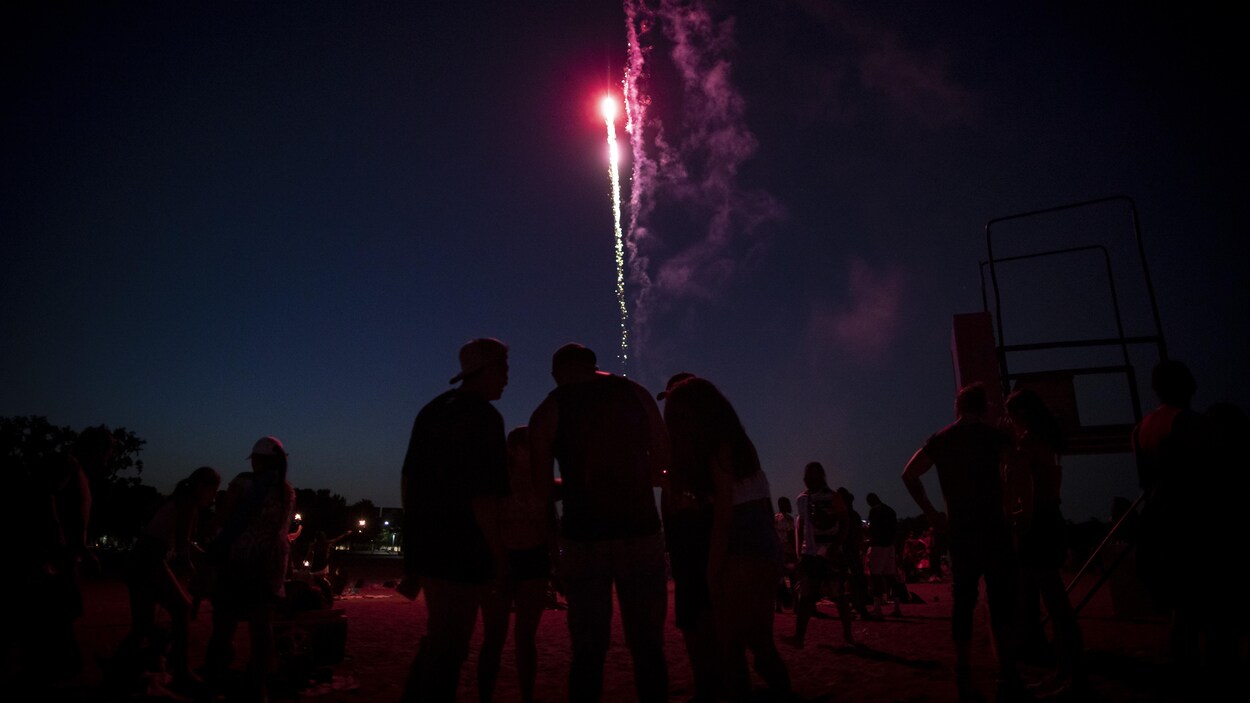 Des personnes rassemblées sur une plage la nuit avec des feux d'artifice dans le ciel.