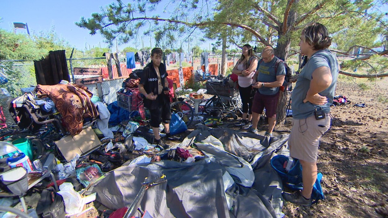 Trois hommes et une femme se tiennent debout devant un parterre d'objets divers. Il s'agit de vêtements et autres objets étalés le long d'une clôture.