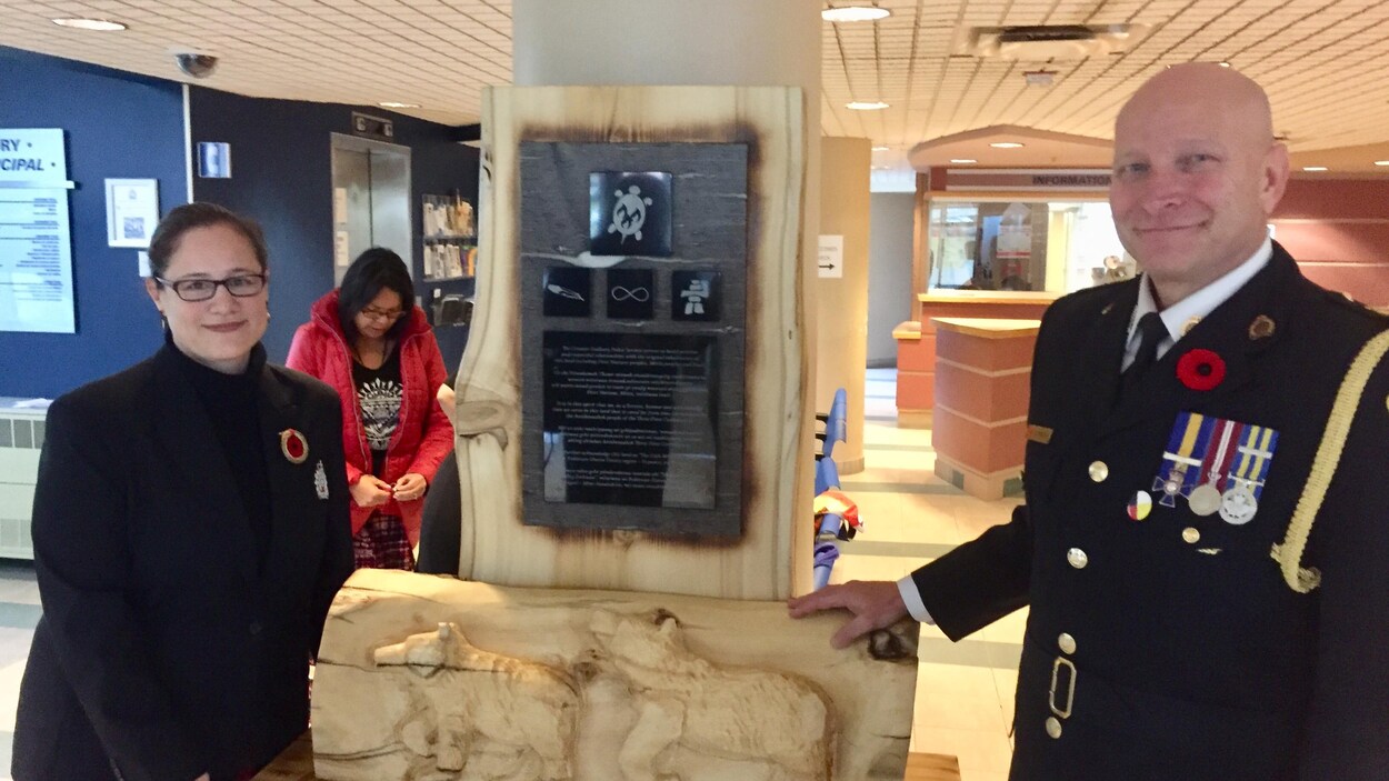 Deux personnes entourant une plaque et une sculpture.