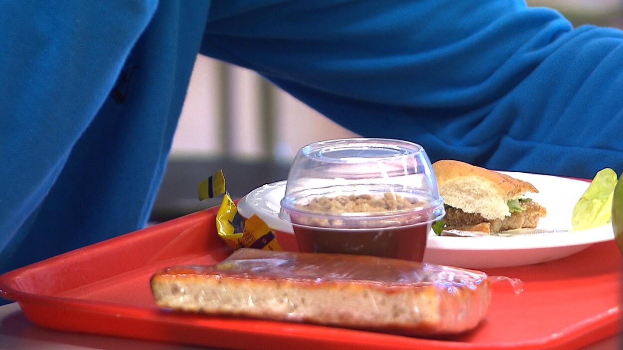 Un élève, dont on voit un bras, est assis devant un plateau d'aliments dans la cafétéria de son école.