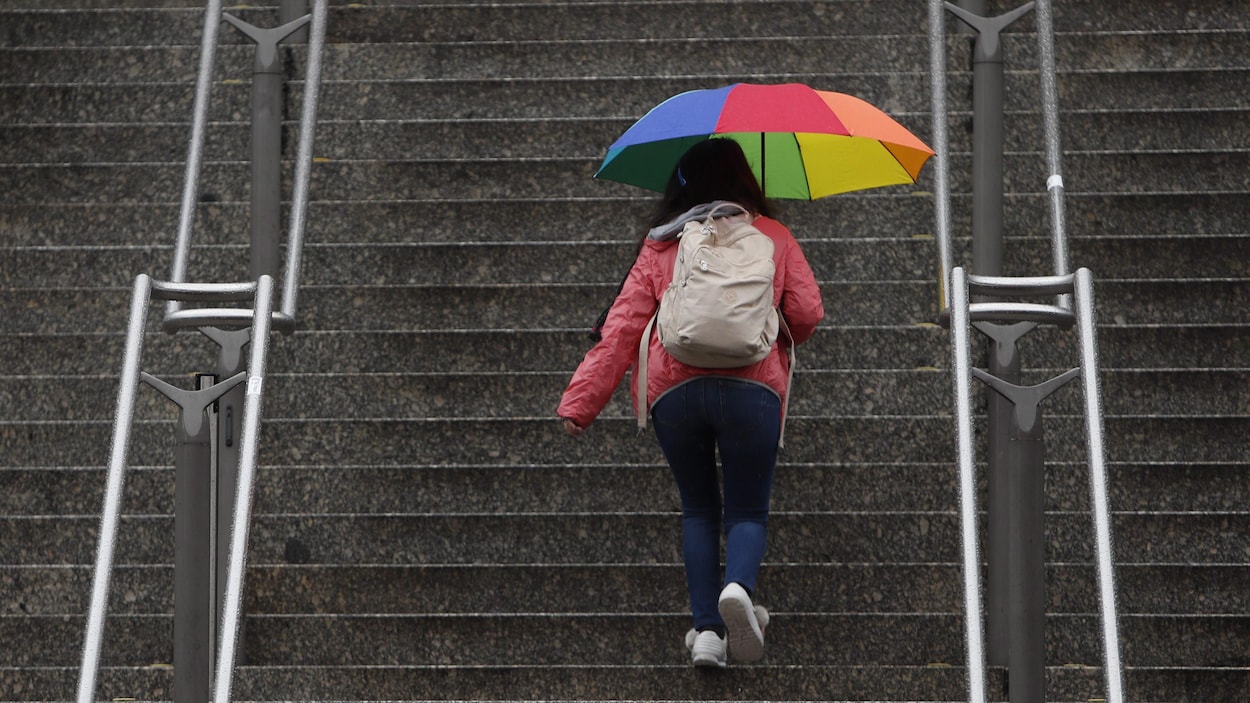 Une femme monte un escalier avec un parapluie multicolore.