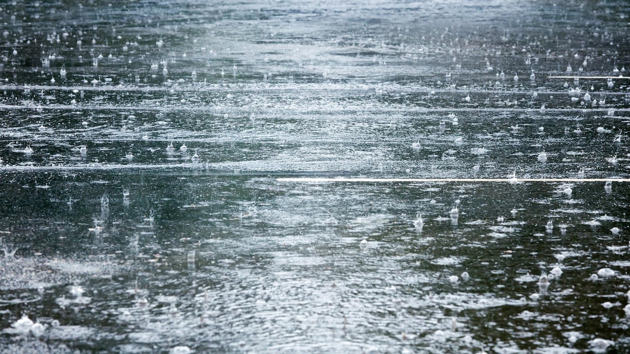Une photo d'une route inondée par la pluie. De nombreuses gouttes tombent du ciel.